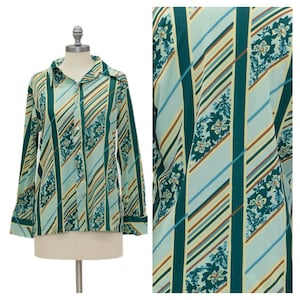May include: A long-sleeve button-down shirt featuring a light blue base with dark green vertical stripes and diagonal stripes in brown, light blue, and white. The shirt includes a floral pattern integrated within the vertical green bands.