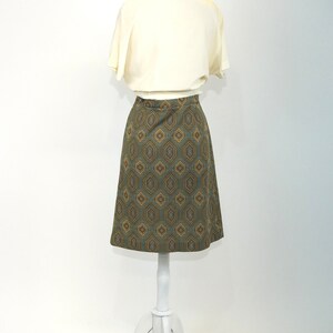 May include: A white blouse with a geometric patterned skirt. The skirt is a-line and has a brown, blue, and gold pattern.