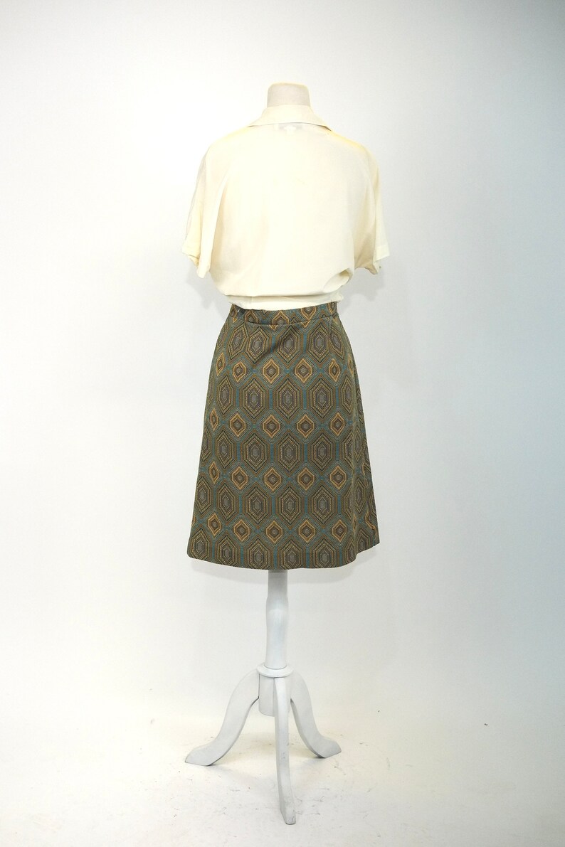 May include: A white blouse with a geometric patterned skirt. The skirt is a-line and has a brown, blue, and gold pattern.