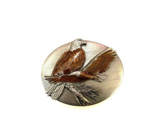 May include: A silver and brown metal pin depicting an eagle perched on a branch. The eagle's feathers are painted in shades of brown and orange.