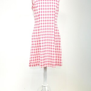 May include: A sleeveless dress with a white background and a pink geometric pattern. The dress has a fitted bodice and a flared skirt.