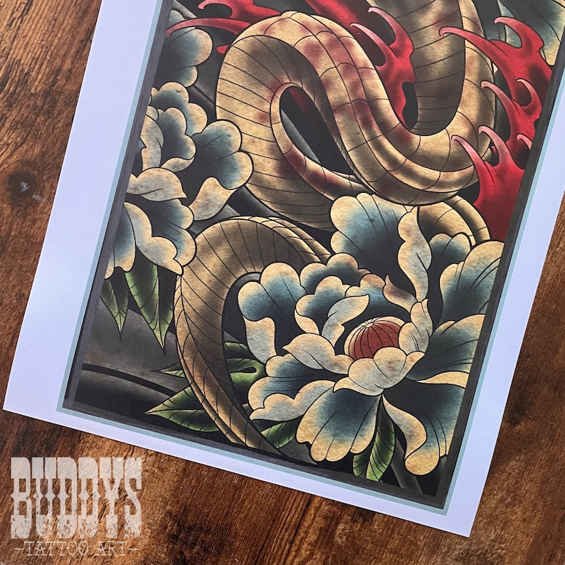 May include: A framed tattoo art print featuring a detailed illustration of a snake intertwined with blue and cream-colored peony flowers. Red accents highlight the design. The print is set against a dark background. The text "BUDDY'S TATTOO ART" is visible at the bottom.