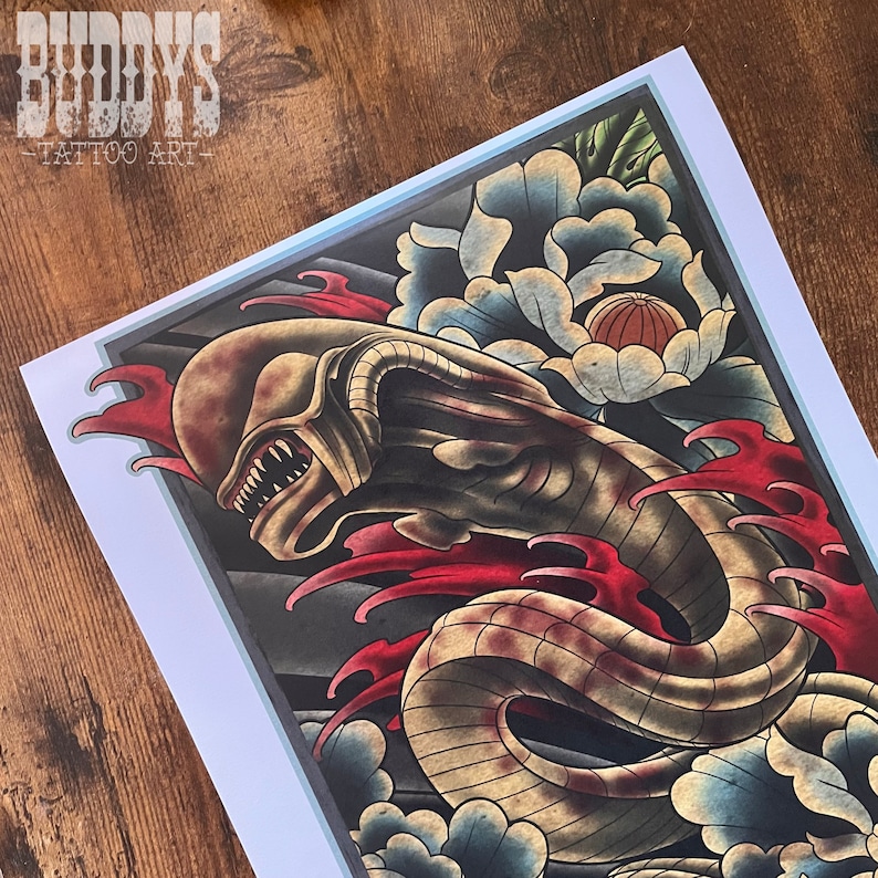 May include: Tattoo art print featuring a detailed illustration of an alien creature with sharp teeth, set against a backdrop of stylized waves and a large flower. The artwork is framed with a light blue border and includes the text "BUDDYS TATTOO ART".