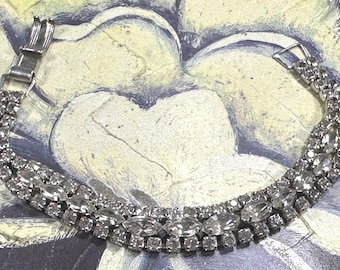 May include: A silver bracelet with a row of clear rhinestones. The bracelet is made of metal and has a clasp closure.