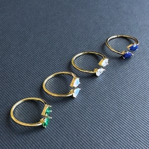 May include: Five gold rings with different coloured gemstones. Each ring has two pear-shaped gemstones. The gemstones are green, white, blue, and a darker blue.