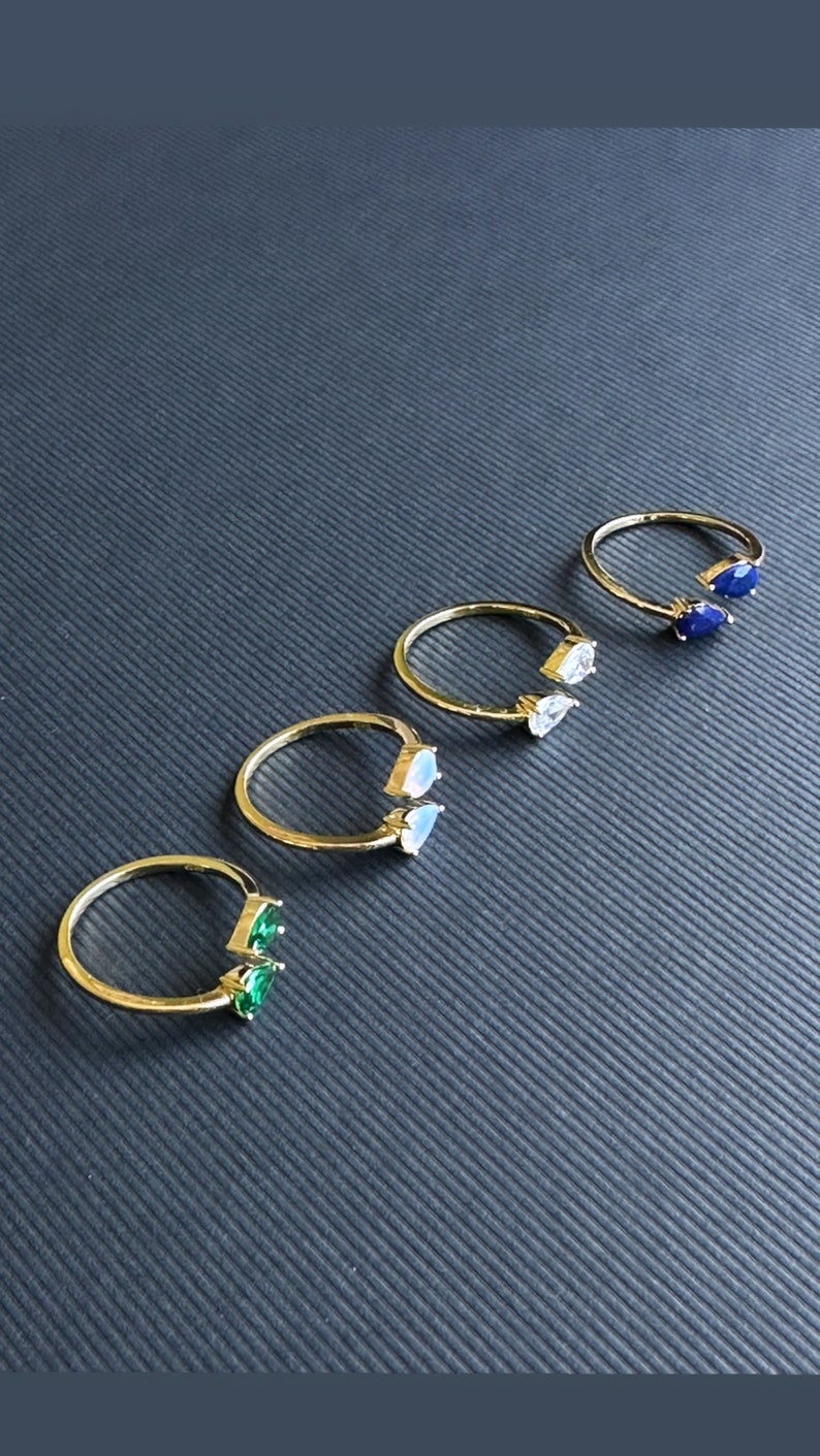 May include: Five gold rings with different coloured gemstones. Each ring has two pear-shaped gemstones. The gemstones are green, white, blue, and a darker blue.