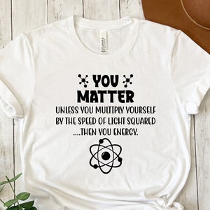 May include: White t-shirt with a black graphic that says "*YOU* MATTER" and "UNLESS YOU MULTIPLY YOURSELF BY THE SPEED OF LIGHT SQUARED.....THEN YOU ENERGY." with an atom symbol below the text.