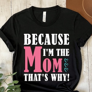 May include: Black t-shirt with white text that reads "Because I'm the Mom That's Why!" The word "Mom" is in pink with blue hearts.