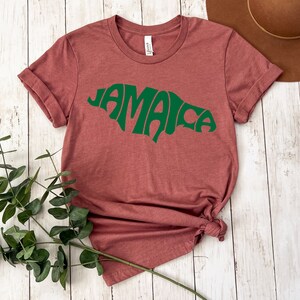 May include: A maroon t-shirt with a green outline of the island of Jamaica and the word "Jamaica" written in a stylized font.