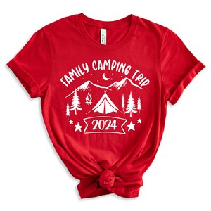 Pu&ograve; includere: Maglietta rossa con testo bianco che dice "Family Camping Trip 2024" con una grafica di una tenda, montagne, alberi e un fal&ograve;.