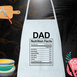 May include: White kitchen apron with a humorous nutrition facts label for "DAD". The label lists various qualities like "Hard Work", "Role Model", and "Unconditional Love", all with a 100% daily value. The apron has a red and white "Good Food" graphic in the bottom right corner.
