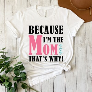 May include: White t-shirt with black text that reads "Because I'm the Mom That's Why!" The word "Mom" is in pink.