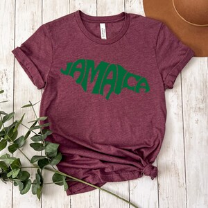 May include: A maroon t-shirt with a green outline of the island of Jamaica and the word "Jamaica" written inside the outline.