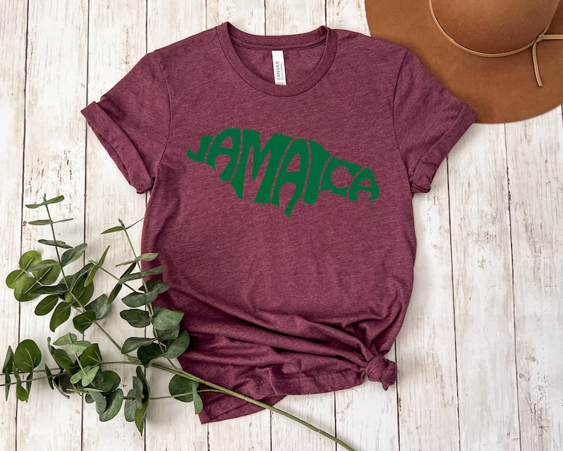 May include: A maroon t-shirt with a green outline of the island of Jamaica and the word "Jamaica" written inside the outline.