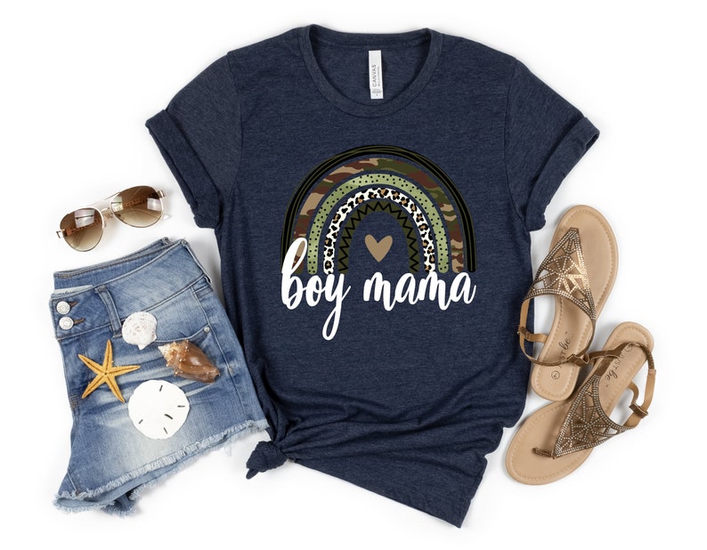 K&ouml;nnte beinhalten: Ein marineblaues T-Shirt mit einem Regenbogen-Design aus Tarnmuster, Leopardenmuster und Punkten. Der Regenbogen hat ein Herz in der Mitte und den Text "boy mama" darunter.