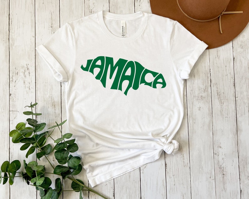 May include: White t-shirt with a green outline of the island of Jamaica, the word "Jamaica" is spelled out within the outline.
