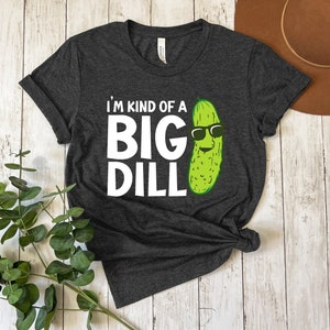 Peut inclure: Un t-shirt gris fonc&eacute; avec le texte "I'm kind of a big dill" en lettres blanches et un cornichon de dessin anim&eacute; portant des lunettes de soleil.