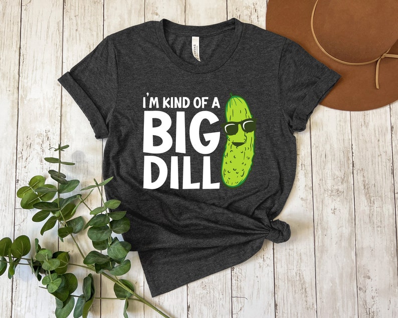 Peut inclure: Un t-shirt gris fonc&eacute; avec le texte "I'm kind of a big dill" en lettres blanches et un cornichon de dessin anim&eacute; portant des lunettes de soleil.