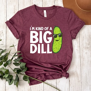 Peut inclure: Un t-shirt marron avec le texte "I'm kind of a big dill" et un cornichon de dessin anim&eacute; portant des lunettes de soleil.
