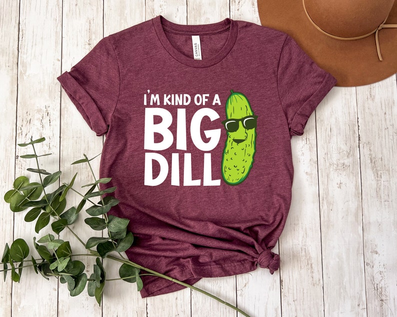 Peut inclure: Un t-shirt marron avec le texte "I'm kind of a big dill" et un cornichon de dessin anim&eacute; portant des lunettes de soleil.