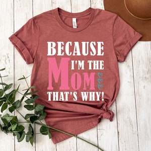 May include: A maroon t-shirt with the text "Because I'm the Mom That's Why!" in white. The word "Mom" is in pink.