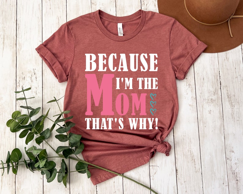 May include: A maroon t-shirt with the text "Because I'm the Mom That's Why!" in white. The word "Mom" is in pink.