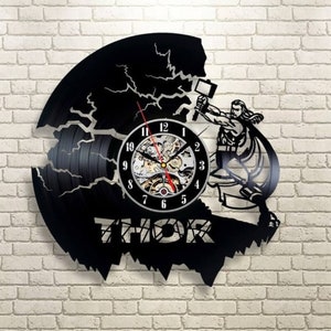 May include: A black vinyl record clock featuring a silhouette of Thor, the Norse god of thunder, wielding his hammer, Mjolnir. The clock face is a circular cutout with Roman numeral markings and a working clock mechanism. The words "THOR" are printed below the clock face.