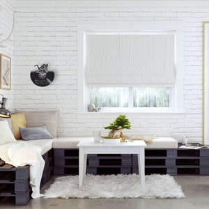 May include: A white pallet couch with a white throw blanket and pillows in a living room with a white brick wall, a white coffee table, a small bonsai tree, and a poster for the Camden Green & Bikefest.