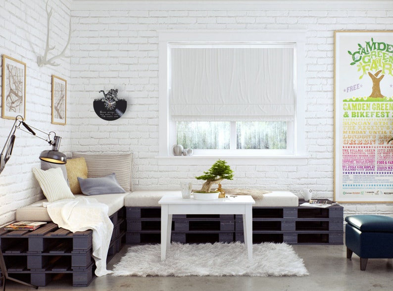 May include: A white pallet couch with a white throw blanket and pillows in a living room with a white brick wall, a white coffee table, a small bonsai tree, and a poster for the Camden Green & Bikefest.