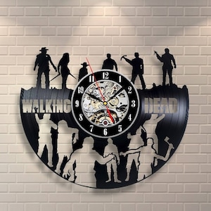 Peut inclure: Horloge en vinyle noir avec des personnages de la série télévisée "The Walking Dead". Le cadran de l'horloge a des chiffres romains et un design d'engrenage argenté. L'horloge est entourée de silhouettes de personnages de la série, dont Rick Grimes, Daryl Dixon et Michonne.