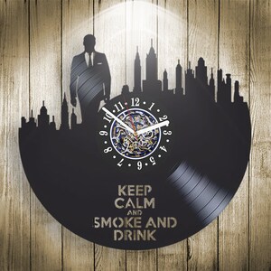 May include: Black vinyl record clock with a cityscape silhouette and a man in a suit. The clock face has Roman numerals and the text "Keep Calm and Smoke and Drink".