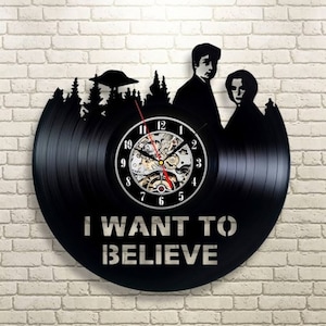 May include: A black vinyl record clock featuring a silhouette of the characters from the movie "The X-Files" with the text "I WANT TO BELIEVE" printed below the clock face.