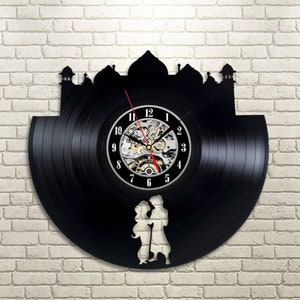 May include: A black vinyl record clock with a silhouette of a mosque and two figures in front of it. The clock face has Roman numerals and a silver clock mechanism.