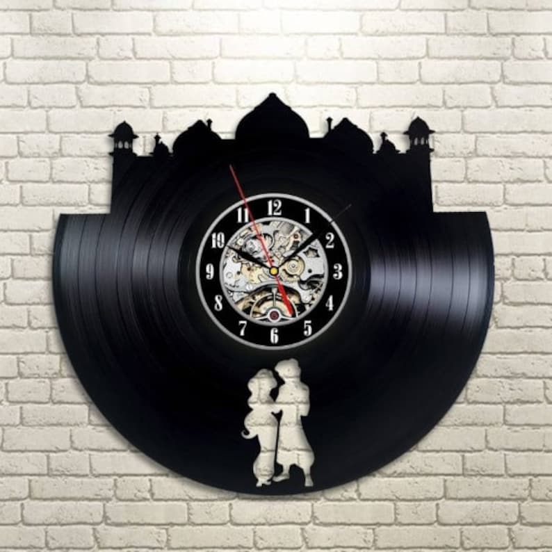 May include: A black vinyl record clock with a silhouette of a mosque and two figures in front of it. The clock face has Roman numerals and a silver clock mechanism.