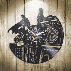 May include: Black vinyl record clock featuring a silhouette of Batman flying over a building with a clock face. The clock face has Roman numerals and a blue and gold clock mechanism.
