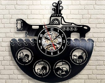 May include: Black vinyl record clock featuring a yellow submarine with a clock face and four smaller circles with images of the Beatles. The clock is mounted on a brick wall.