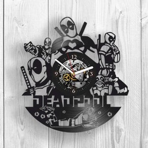 Op de afbeelding: Zwarte vinyl platen klok met een silhouet van Deadpool-karakters. De wijzerplaat is een zilver en zwart tandwiel ontwerp met zwarte wijzers. De klok heeft de tekst "DEADPOOL" gedrukt onder de wijzerplaat.