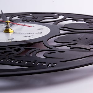 May include: Black vinyl record clock with a white clock face and black hands. The clock face has black Roman numeral markings. The clock is decorated with a black, intricate design.