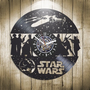 Pode incluir: Um relógio de vinil preto com tema Star Wars. O mostrador do relógio é um círculo branco com números e ponteiros pretos. O relógio é cercado por uma silhueta preta de personagens dos filmes Star Wars, incluindo Darth Vader, Luke Skywalker e a princesa Leia. O relógio também apresenta uma silhueta da nave espacial Millennium Falcon.