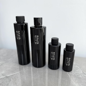 May include: Four black bottles with black caps and white labels that read "DIAD EVIL" in a gothic font. The bottles are arranged in a row from largest to smallest on a grey surface.