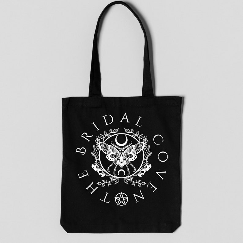 May include: Black tote bag with a white graphic of a moth, crescent moon, and pentagram inside a wreath. The text "The Bridal Coven" is written around the graphic.