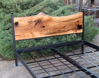 Könnte beinhalten: Ein schwarzes Metallbettgestell mit einem Holz-Kopfteil. Das Kopfteil besteht aus einem einzigen Stück Holz mit einer natürlichen Kante und einer rustikalen Oberfläche.