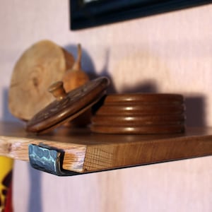 Könnte beinhalten: Ein Holzregal mit dunkler Oberfläche, getragen von einer gehämmerten Metallhalterung. Auf dem Regal befinden sich dekorative Holzgegenstände, darunter ein runder Behälter mit Deckel, eine Kerze und eine Holzscheibe. Das Regal ist an einer rosa Wand befestigt.
