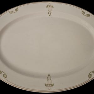 Puede incluir: Plato ovalado de color crema con un fino borde dorado y detalles florales verdes decorativos. El plato tiene una superficie lisa y es adecuado para servir alimentos. Una pieza clásica para cualquier ocasión.