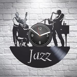 May include: Black vinyl record clock featuring a silhouette of a jazz band playing saxophone, bass, and drums. The clock face is black with white numbers and hands. The record is labeled "Jazz".