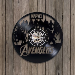 May include: Black vinyl record clock featuring a silhouette of the Avengers characters from Marvel Comics. The clock face has a white background with black numbers and hands. The words "MARVEL" and "AVENGERS" are printed on the clock face.