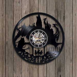 May include: Black vinyl record clock featuring a silhouette of Hogwarts castle and characters from the Harry Potter series. The clock face is a clear circle with black numbers and hands. The clock has a black metal frame and a black background.
