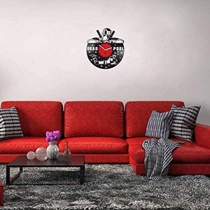 May include: A black vinyl record clock featuring a silhouette of Deadpool with the words "DEAD POOL" printed on the record. The clock hands are red and the background is black.