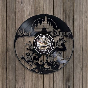 May include: Black vinyl record clock featuring a Disney theme. The clock has a central clock face with visible gears, surrounded by Disney characters and the words "Walt Disney". The clock is mounted on a wooden background.