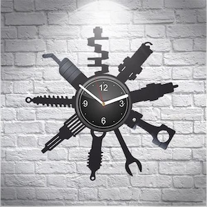 Peut inclure: Horloge murale noire et blanche avec un cadran circulaire et des aiguilles noires. Le cadran est entouré de différentes pièces de voiture, notamment un vilebrequin, des bougies d'allumage et des clés.